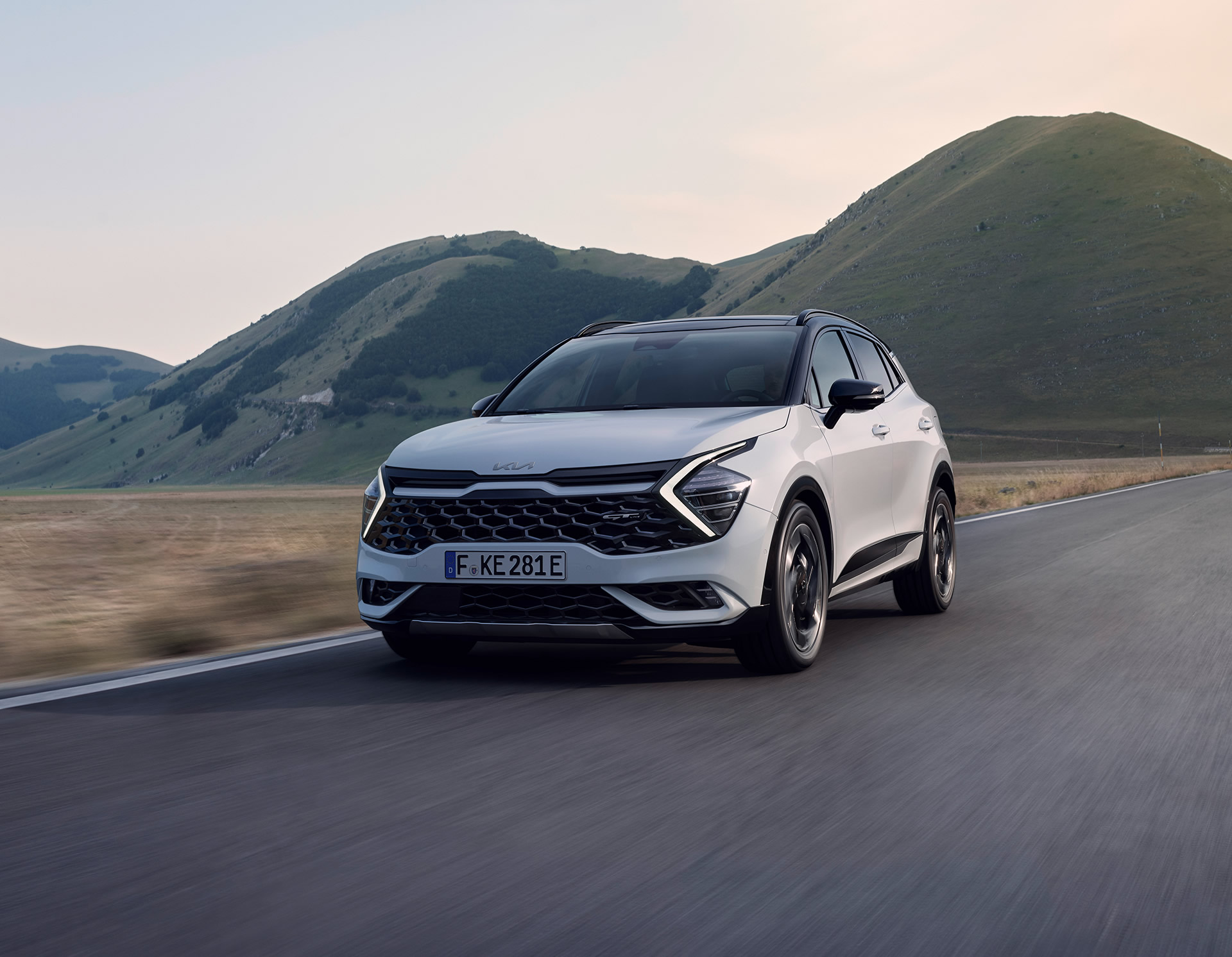 Kia Sportage PHEV, weiß, Frontansicht, Fahrt durch Landschaft